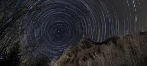 Scia di stelle in rotazione nel cielo notturno sopra le montagne, catturata con tecnica di astrofotografia a lunga esposizione - Fotografia di Montagna: astrofotografia